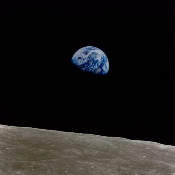 “Earthrise” photograph showing the blue-and-white Earth emerging above the gray, cratered surface of the Moon against the blackness of space.
