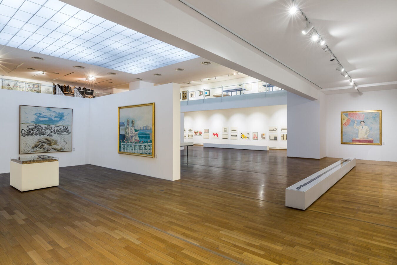Open gallery space in the Ion Bitzan retrospective featuring large-scale paintings, works on paper, and exhibition displays illuminated by skylights and track lighting.