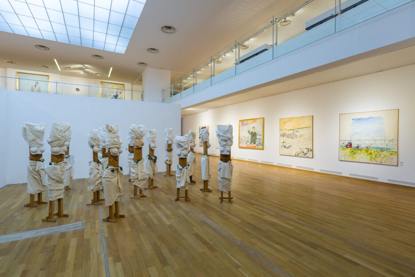 Installation view featuring a group of draped sculptural forms surrounded by large paintings in the Ion Bitzan retrospective at the National Museum of Contemporary Art.
