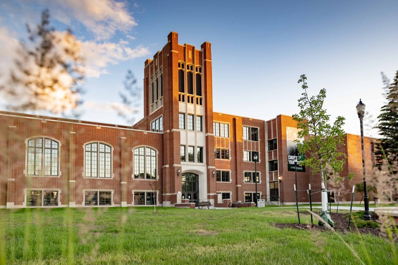 Color photograph of a large brick academic building with a central tower, viewed across a grassy lawn under a clear evening sky.