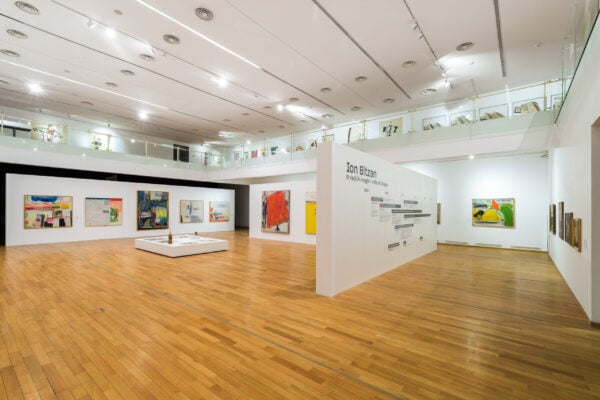 Wide view of the Ion Bitzan retrospective at the National Museum of Contemporary Art in Bucharest, showing large paintings displayed around a central exhibition wall featuring a timeline and interpretive text.