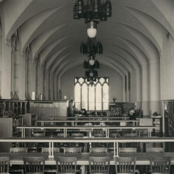 Black-and-white photograph of a library reading room with long study tables, bookshelves, and vaulted ceilings.