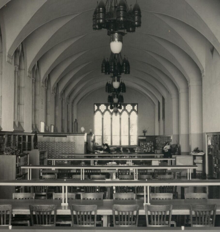 Black-and-white photograph of a library reading room with long study tables, bookshelves, and vaulted ceilings.
