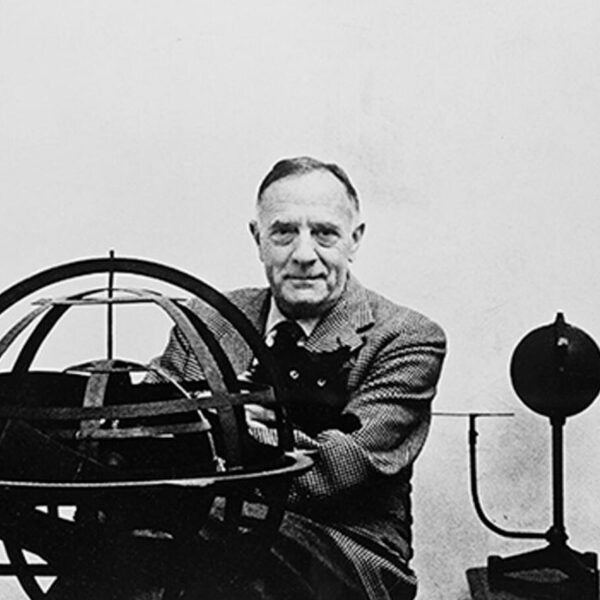 Black-and-white photograph of a man posing beside a large armillary sphere or astronomical instrument.