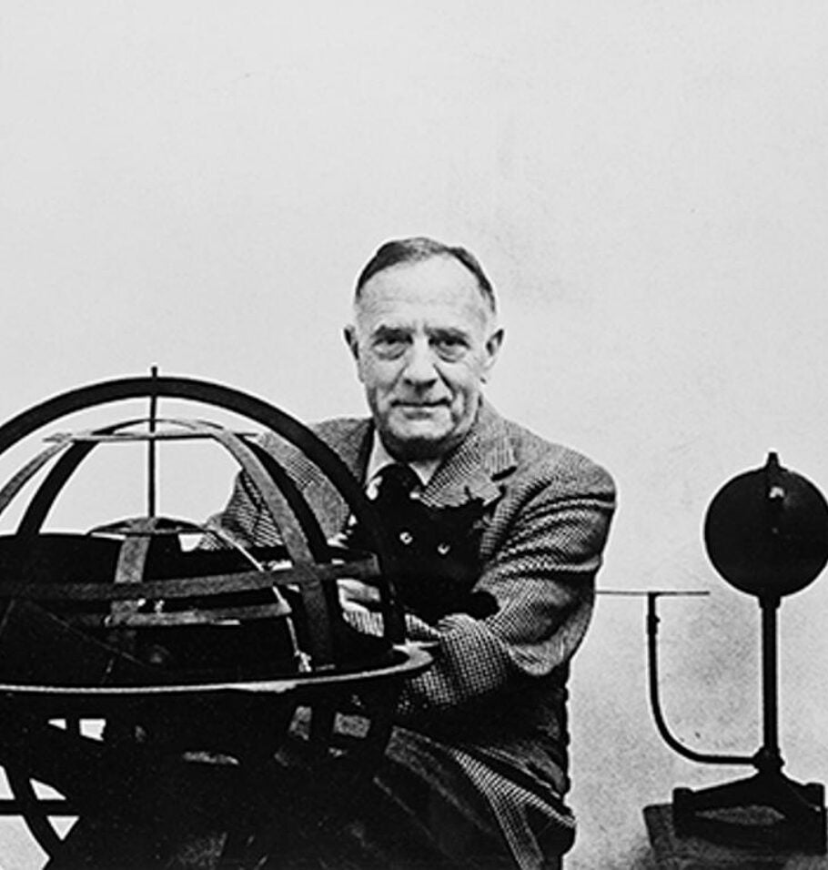 Black-and-white photograph of a man posing beside a large armillary sphere or astronomical instrument.