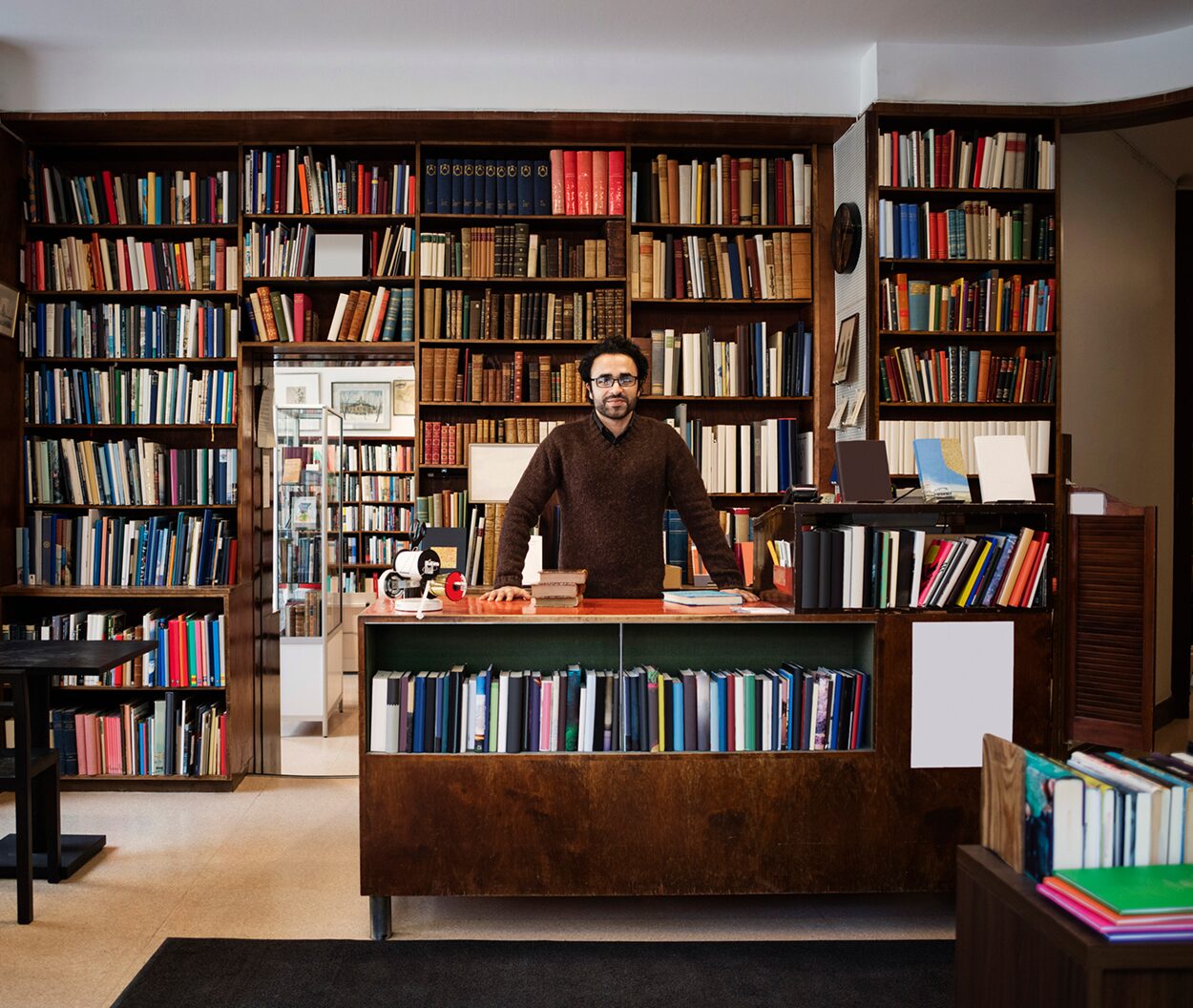 Man standing behind a desk in a book-lined library or office.
