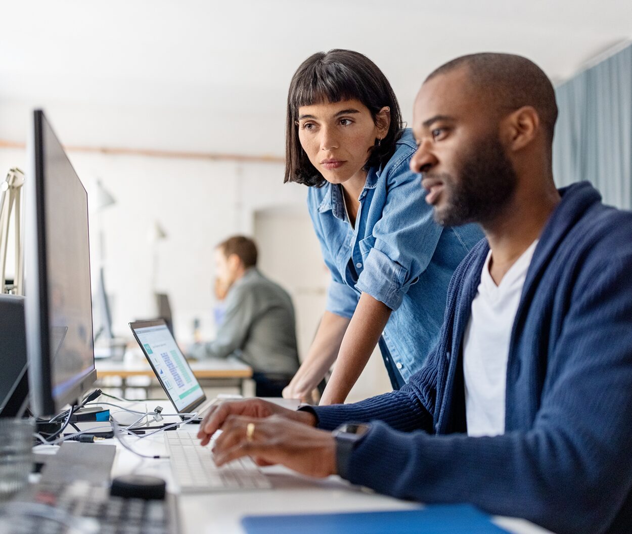 Two colleagues collaborating at a computer, with one leaning in to review the screen.