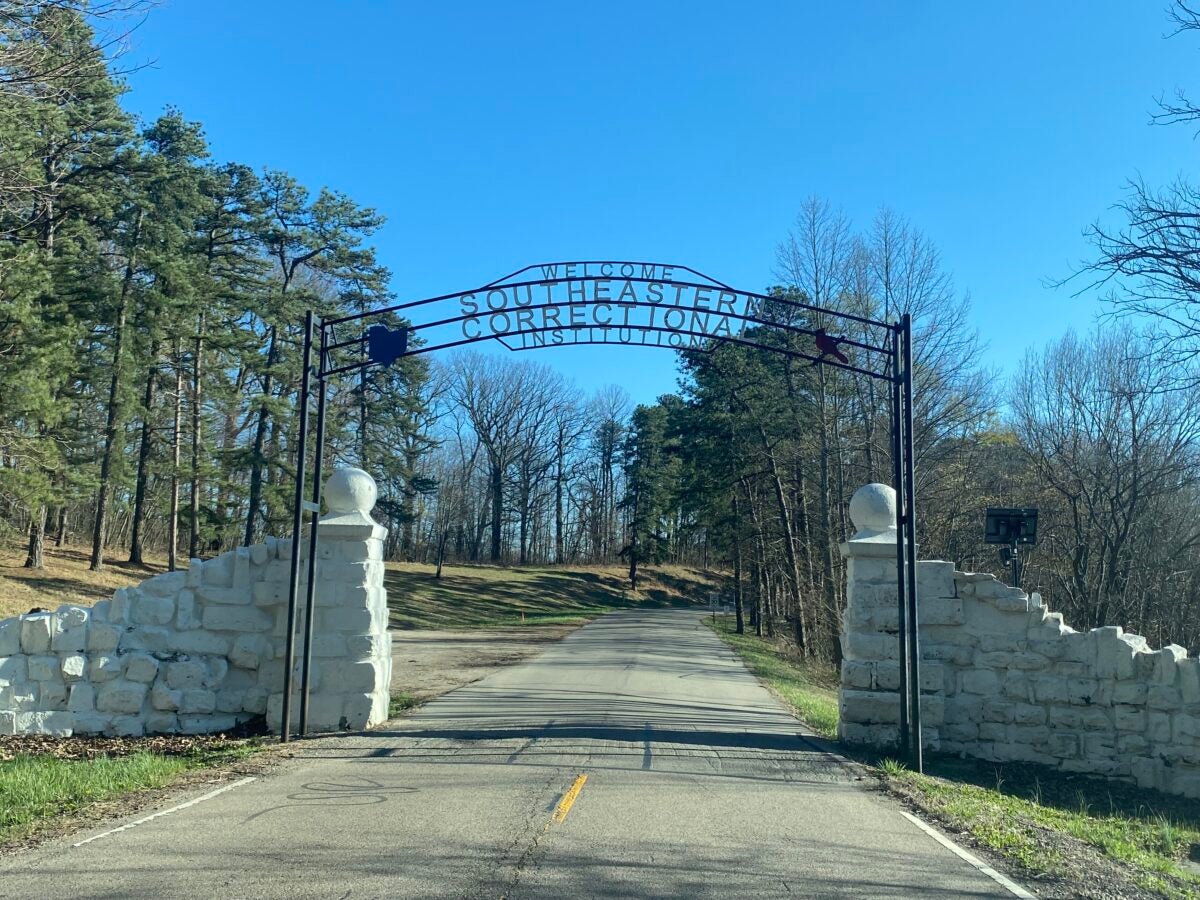 An iron gate over a narrow road that reads “Welcome Southeastern Correctional Institution”.