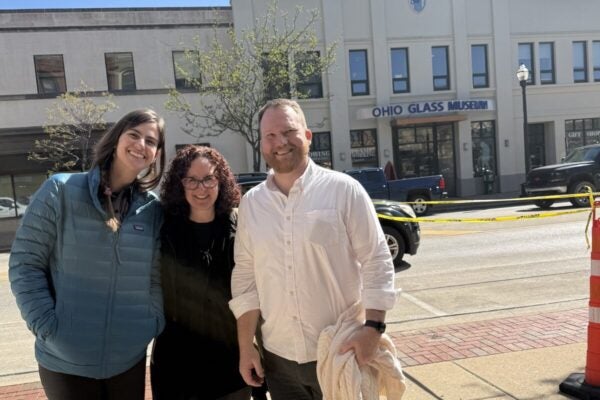 Three people smiling on a sunny day in front of a building that says “Ohio Glass Museum”.