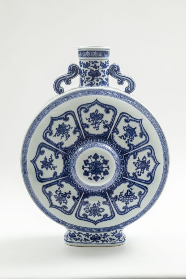 Round white porcelain flask decorated in cobalt blue, with eight Buddhist emblems arranged in panels around a central medallion. A narrow cylindrical neck rises between two curled handles.