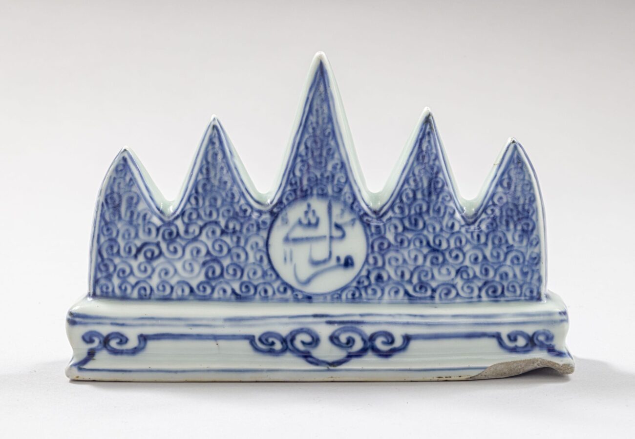 Blue-and-white porcelain brush rest shaped like five pointed mountain peaks. Dense blue scrollwork covers the peaks, with a circular panel containing calligraphic decoration at the center.