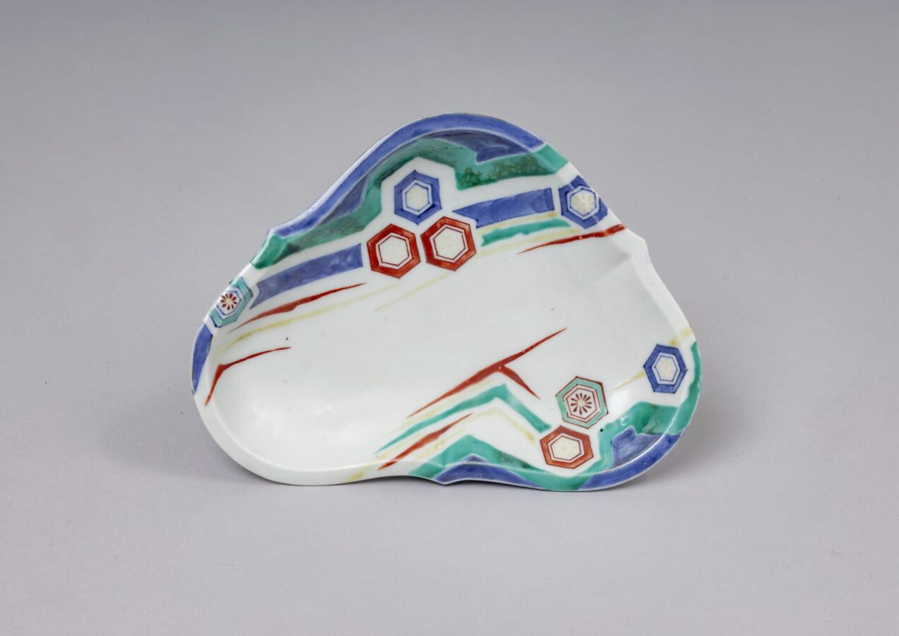 Irregular triangular porcelain dish decorated with sweeping blue, green, red, and yellow lines and clusters of geometric motifs along the edges.