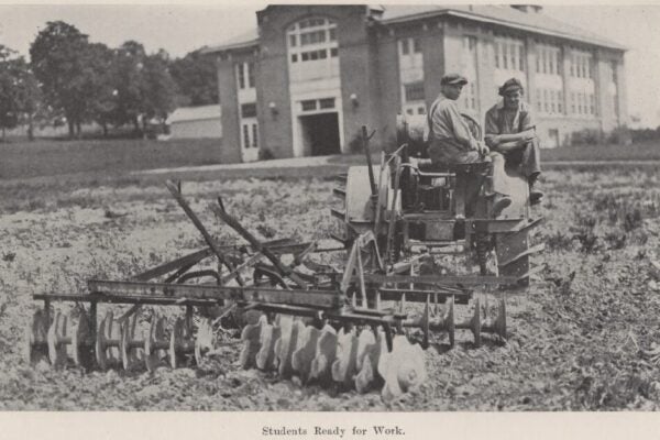 Black-and-white photograph of two students operating farm equipment in a cultivated field at Morrisville in 1926, with Hamilton Hall visible behind them.