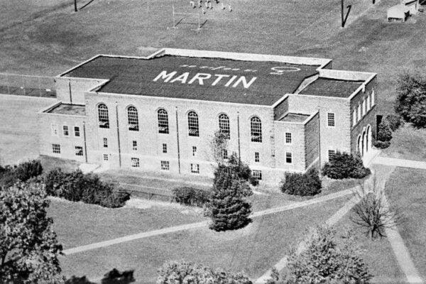 Aerial black-and-white photograph of a large brick campus building with “MARTIN” painted across the roof, surrounded by lawns, trees, and intersecting walkways.
