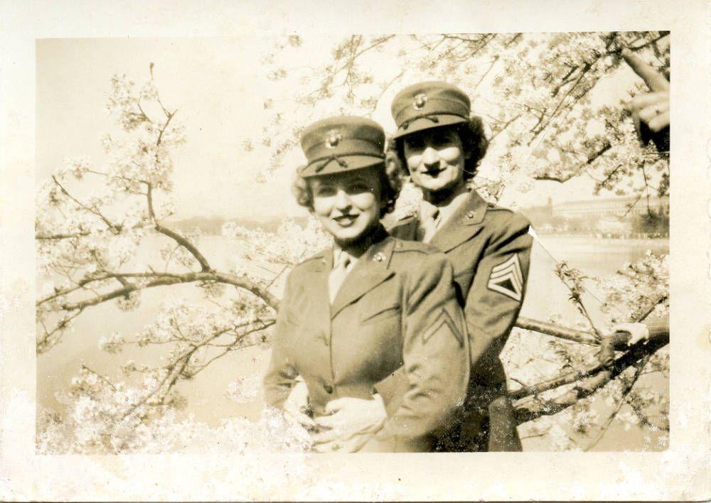 Black-and-white photograph of two women in military uniforms embracing beneath blooming cherry trees.
