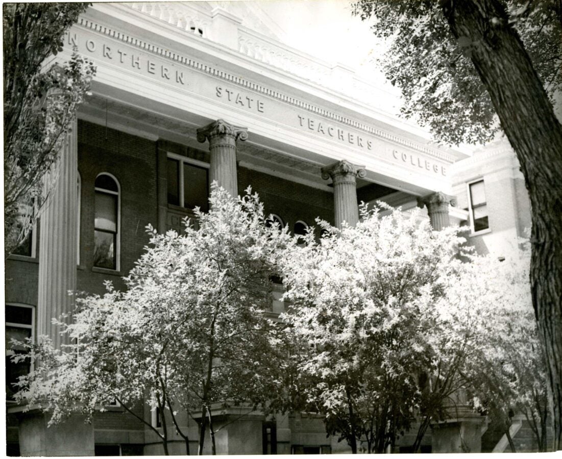 Black-and-white photograph of the Northern State Teachers College building, featuring tall columns and trees partially obscuring the facade.