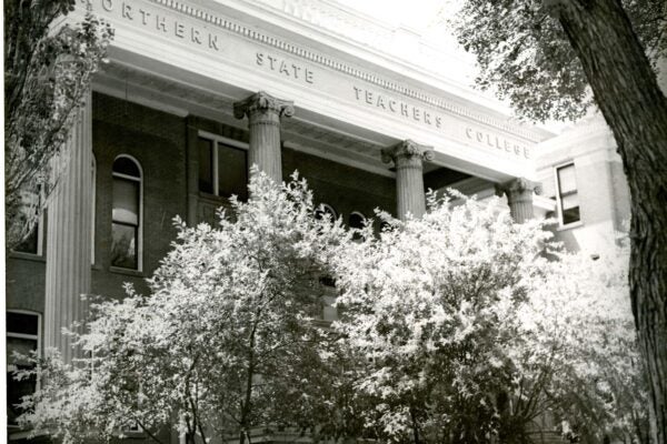 Black-and-white photograph of the Northern State Teachers College building, featuring tall columns and trees partially obscuring the facade.